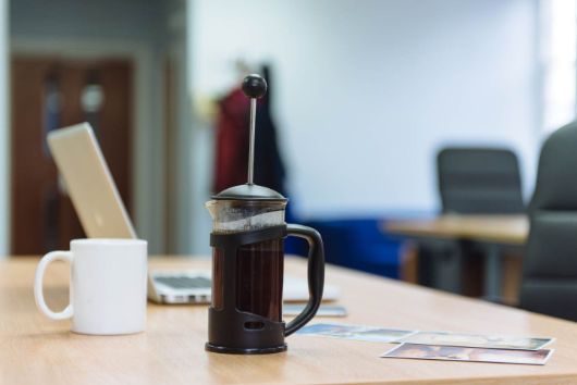 Coffee mug, percolator on desk with laptop behind